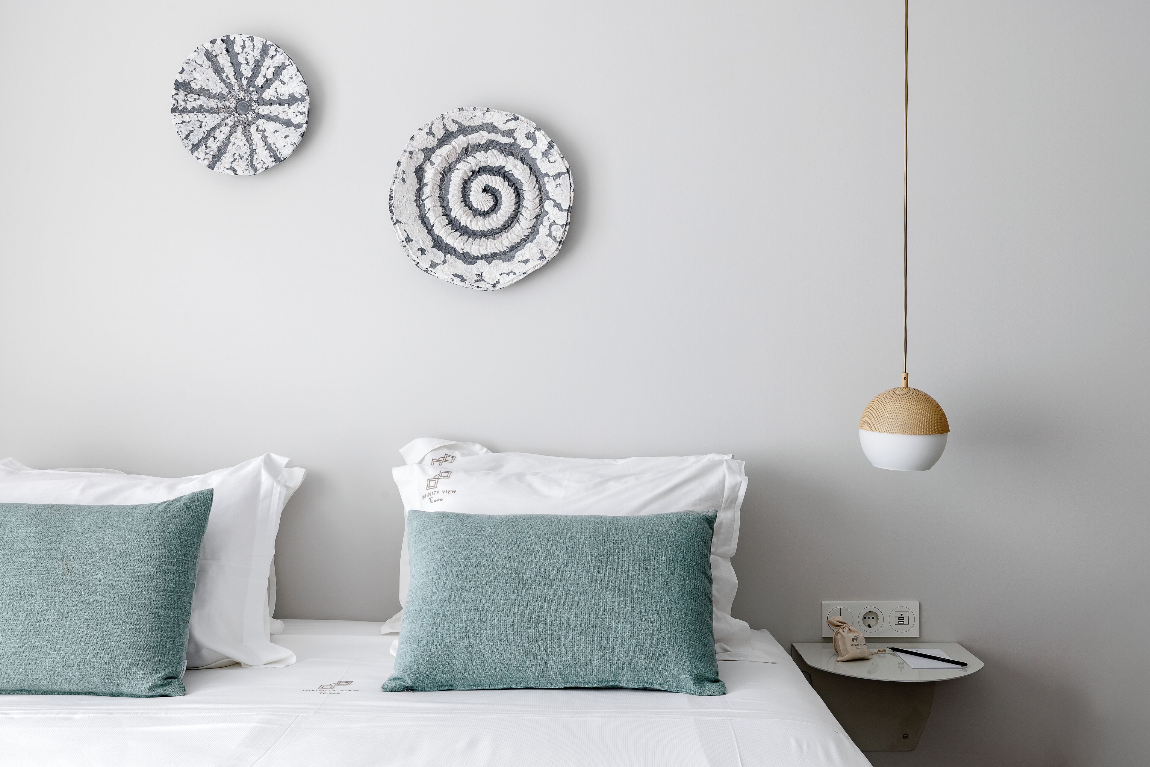 A bedroom with a bed, two pillows, a bedside table, a lamp, and two wall decorations.