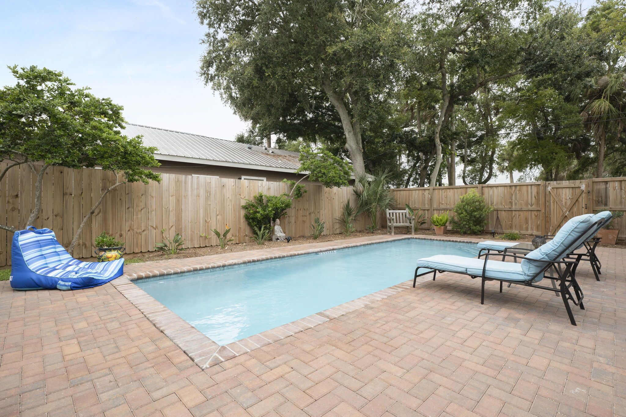 A backyard with a swimming pool, two lounge chairs, a blue bean bag chair, and a wooden fence.