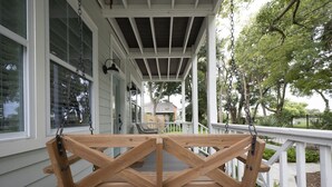 A wooden swing set on a covered porch with white railings and a view of the backyard.