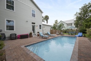A backyard with a swimming pool, lounge chairs, and a wooden deck.