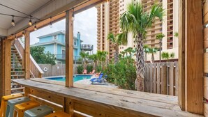 A poolside bar with wooden seating and a view of a pool and palm trees. - Sand Castle ~ 3-Story Beach Retreat with Heated Pool, Tiki Bar & Dual Game Rooms (Panama City Beach)