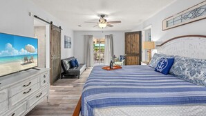 A bedroom with a bed, a TV, a sofa, a ceiling fan, and a view of the outdoors. - Sand Castle ~ 3-Story Beach Retreat with Heated Pool, Tiki Bar & Dual Game Rooms (Panama City Beach)