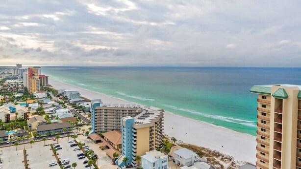 A coastal hotel with a beach view, multiple buildings, and a parking lot. - Sand Castle ~ 3-Story Beach Retreat with Heated Pool, Tiki Bar & Dual Game Rooms (Panama City Beach)