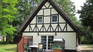 Una casa tradicional con entramado de madera y techo de paja, una terraza de madera y un pequeño espacio al aire libre con sillas y una mesa.