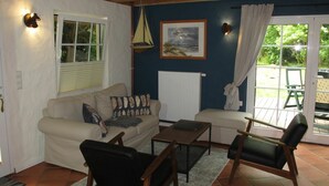 Una sala de estar acogedora con sofá, sillas, una mesa y vista al jardín a través de un ventanal corredero.