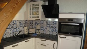 Una cocina con armarios blancos, encimera negra, cafetera, tostadora y horno empotrado.