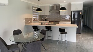 Et moderne køkken med en central ø, barstole og et spisebord i glas.