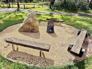 A circular outdoor seating area with a stone centerpiece, benches, and a metal grill.