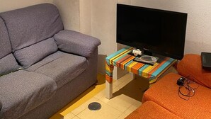 Una sala pequeña con un sofá gris, una mesa colorida a rayas y un sofá naranja.