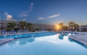 Piscina com espreguiçadeiras e palmeiras, rodeada por edifícios.