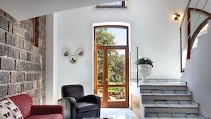 A spacious living area with a stone wall, a large wooden door leading to a garden, a staircase, and a seating area with a red patterned sofa and a black leather chair. - Beautiful private villa with A/C, private pool, WIFI, TV, patio, panoramic view, close to Sorrento (Sant'agata Sui Due Golfi)