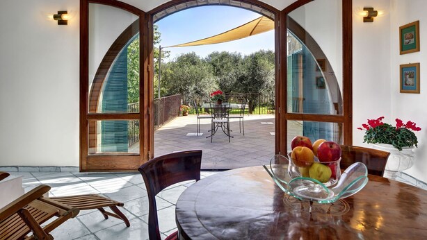 A dining area with a glass table and chairs, a fruit bowl, and a view of an outdoor patio with a table and chairs. - Beautiful private villa with A/C, private pool, WIFI, TV, patio, panoramic view, close to Sorrento (Sant'agata Sui Due Golfi)