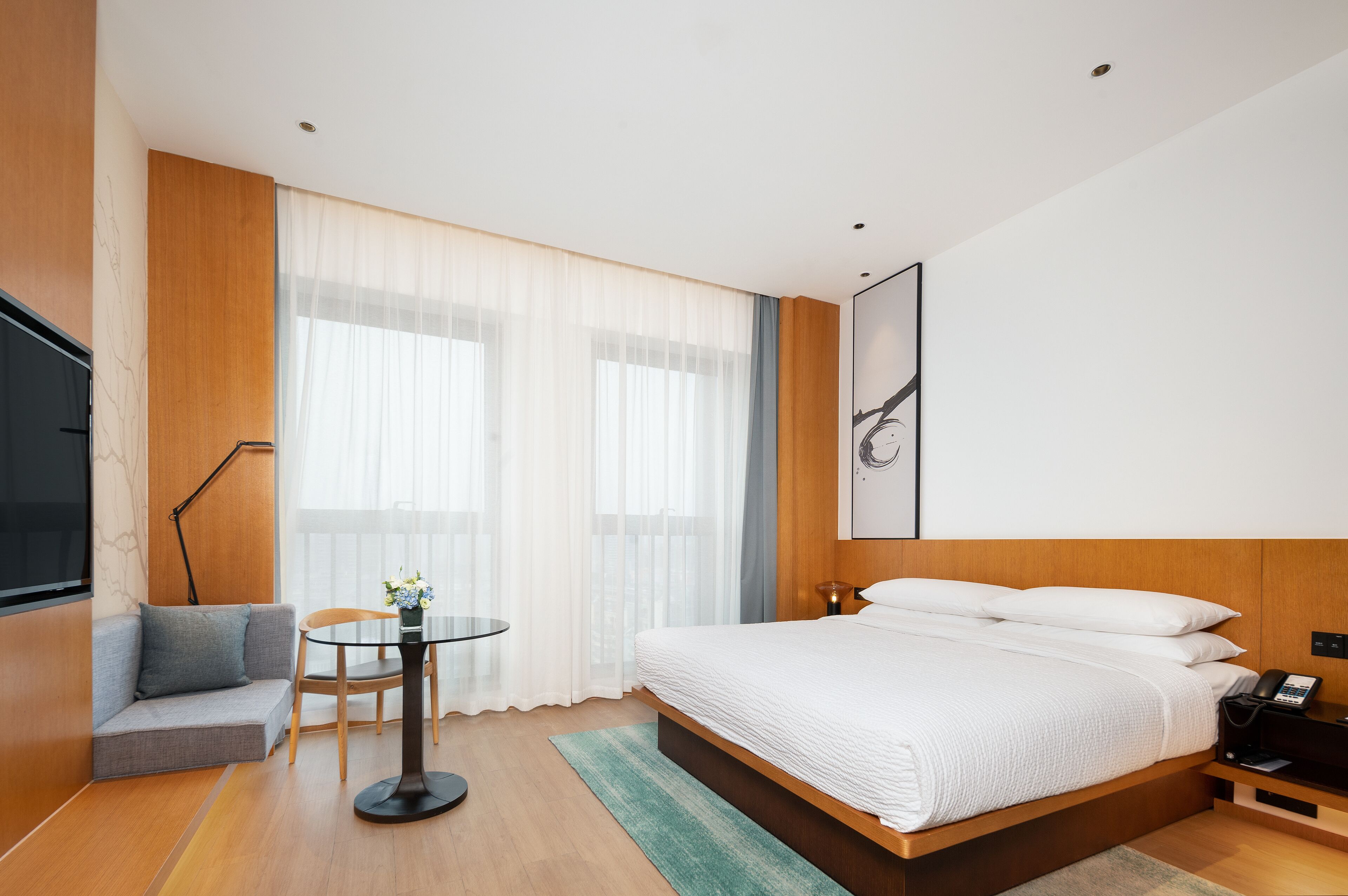 Una habitación de hotel moderna con una cama grande, un sofá, una mesita y un televisor.