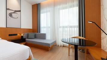 Una habitación de hotel moderna con cama, sofá, una mesita y un ventanal con cortinas.