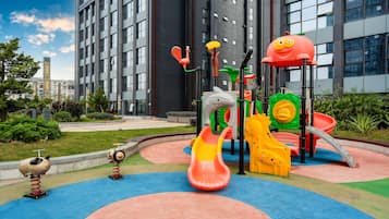 Children can play safely on the rubber surface amidst colorful play structures and lush landscaping.