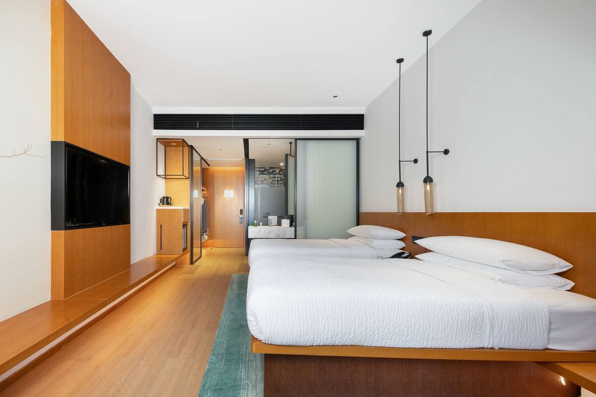 A modern hotel room with a large bed, a television, and a bathroom visible through an open door.