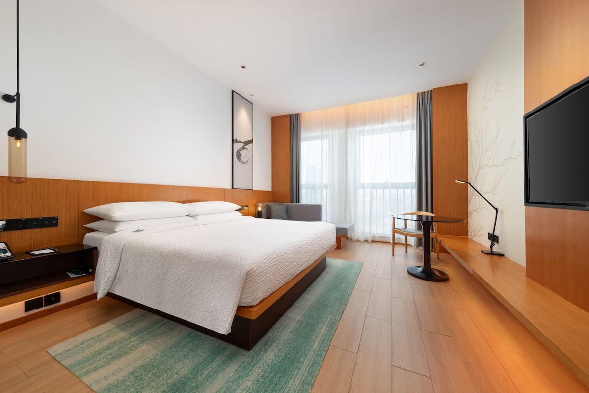 A modern hotel room with a large bed, a desk, and a television.