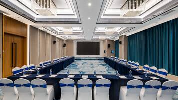 Un salón de conferencias con una mesa larga, sillas con cintas azules y una pantalla grande al frente.