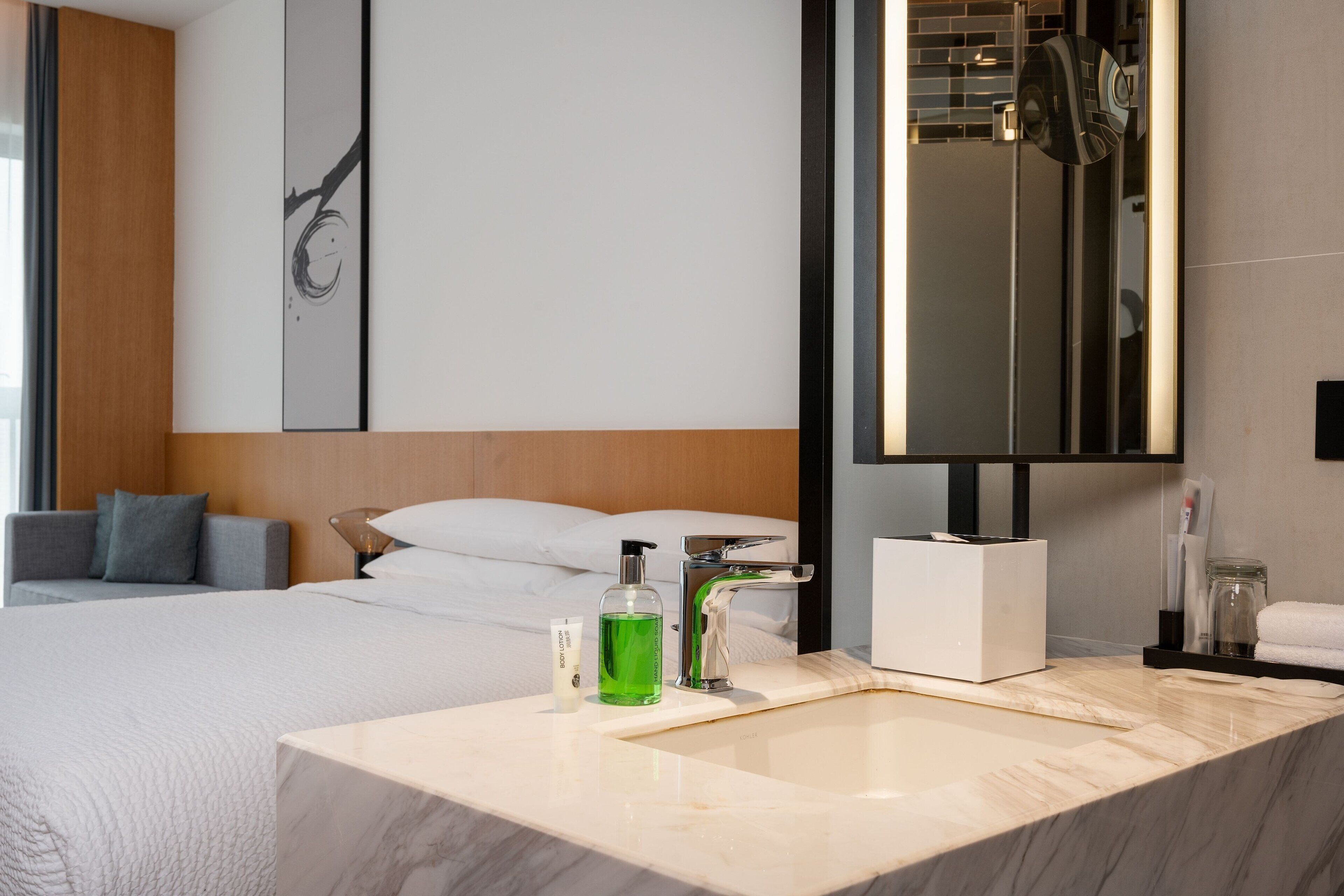 Una habitación de hotel moderna con una cama grande, un baño con lavamanos de mármol y un espejo amplio.