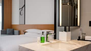 Una habitación de hotel moderna con una cama grande, un baño con lavamanos de mármol y un espejo amplio.