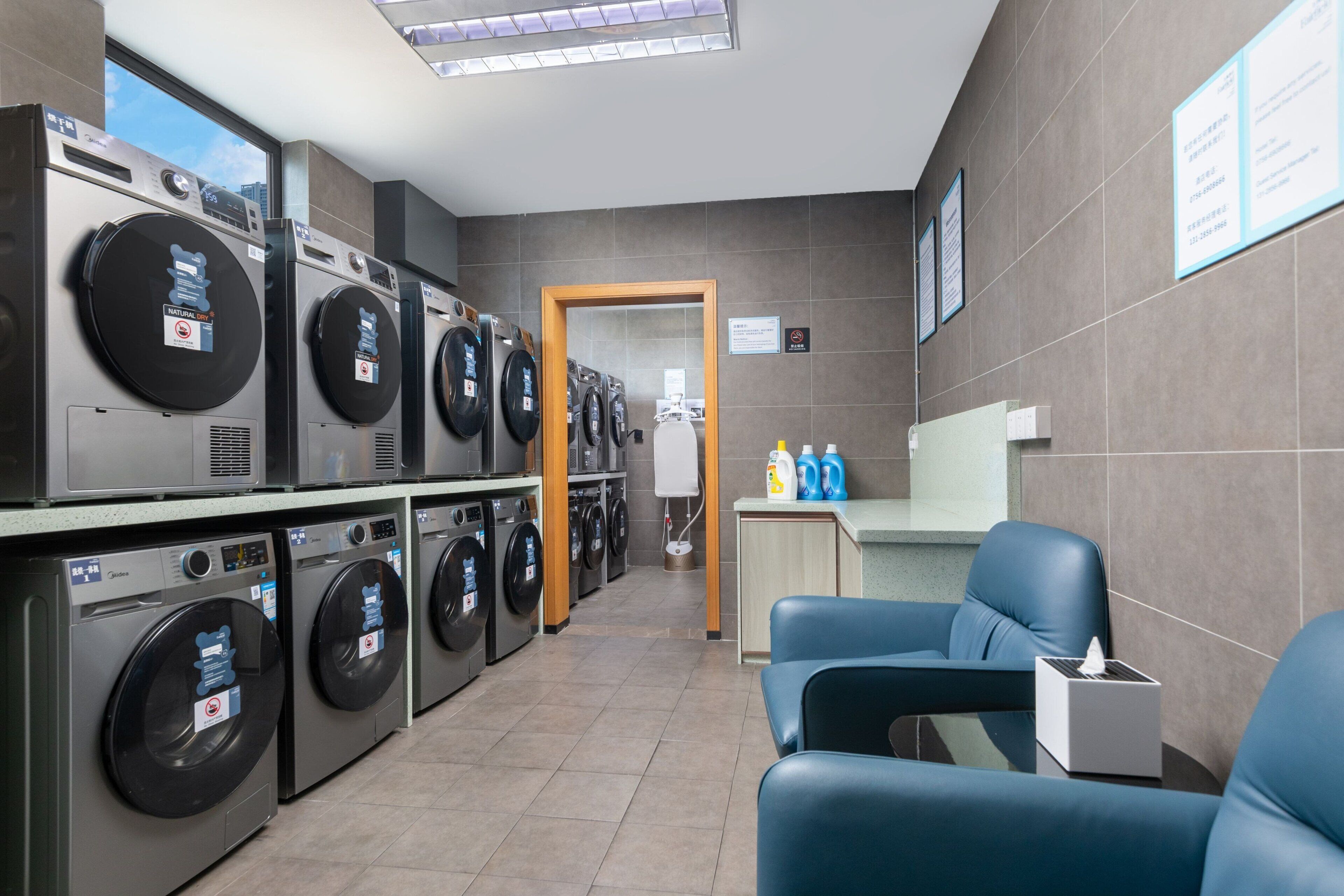 A laundry facility with multiple washing machines, a seating area with blue chairs, and a reception desk.