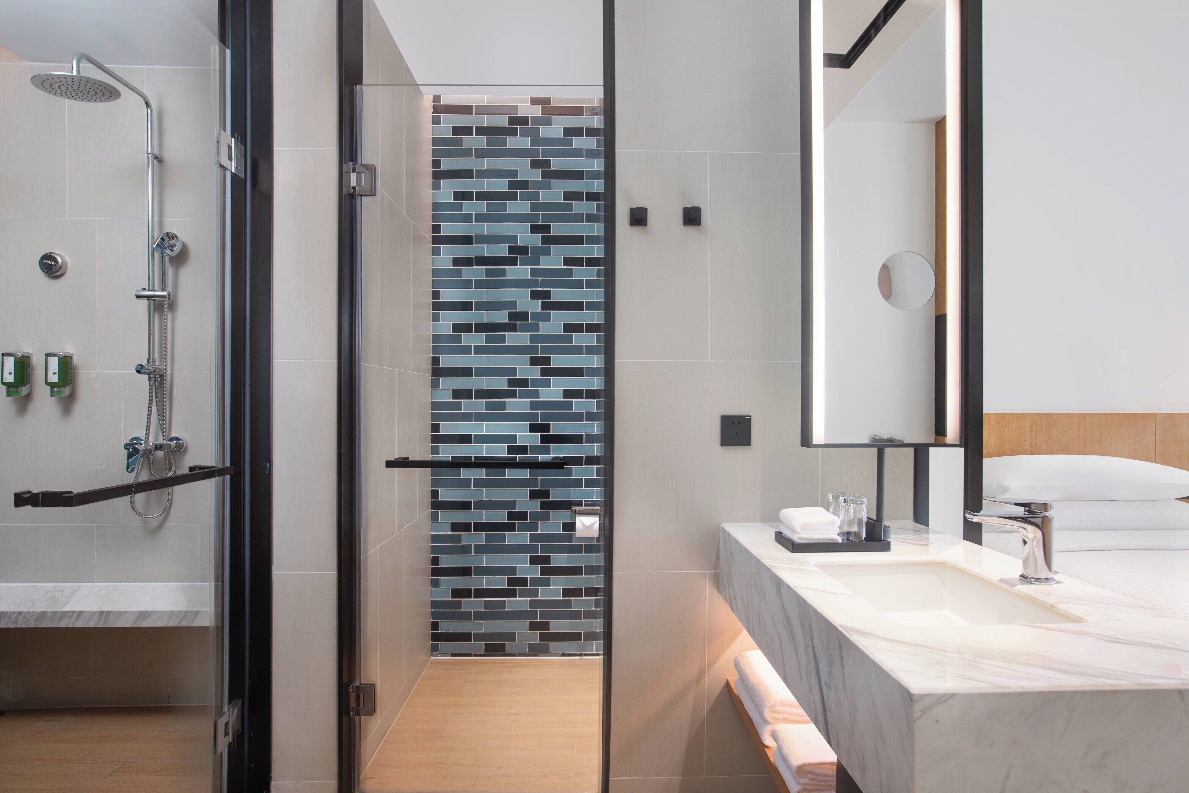 A modern bathroom with a shower, a tiled wall, a sink, and a mirror.