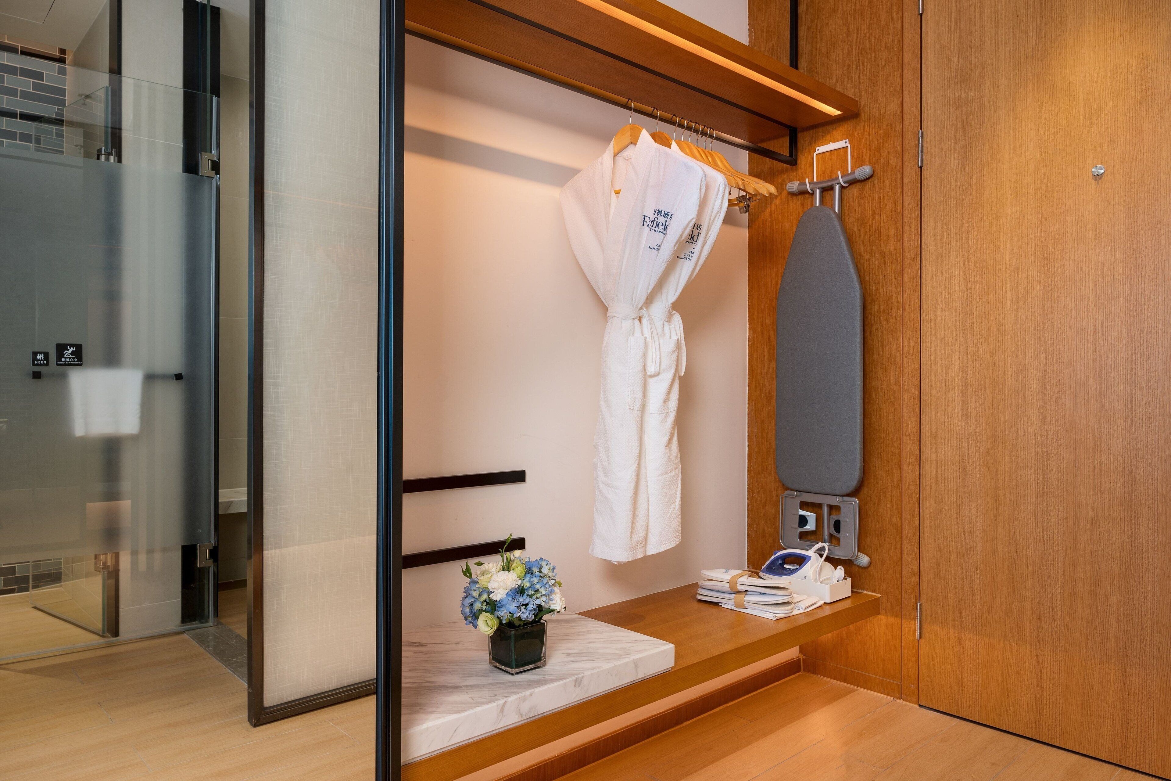 A modern bathroom with a wooden vanity, a towel rack with a robe, a shower area, and a marble-topped shelf with toiletries.
