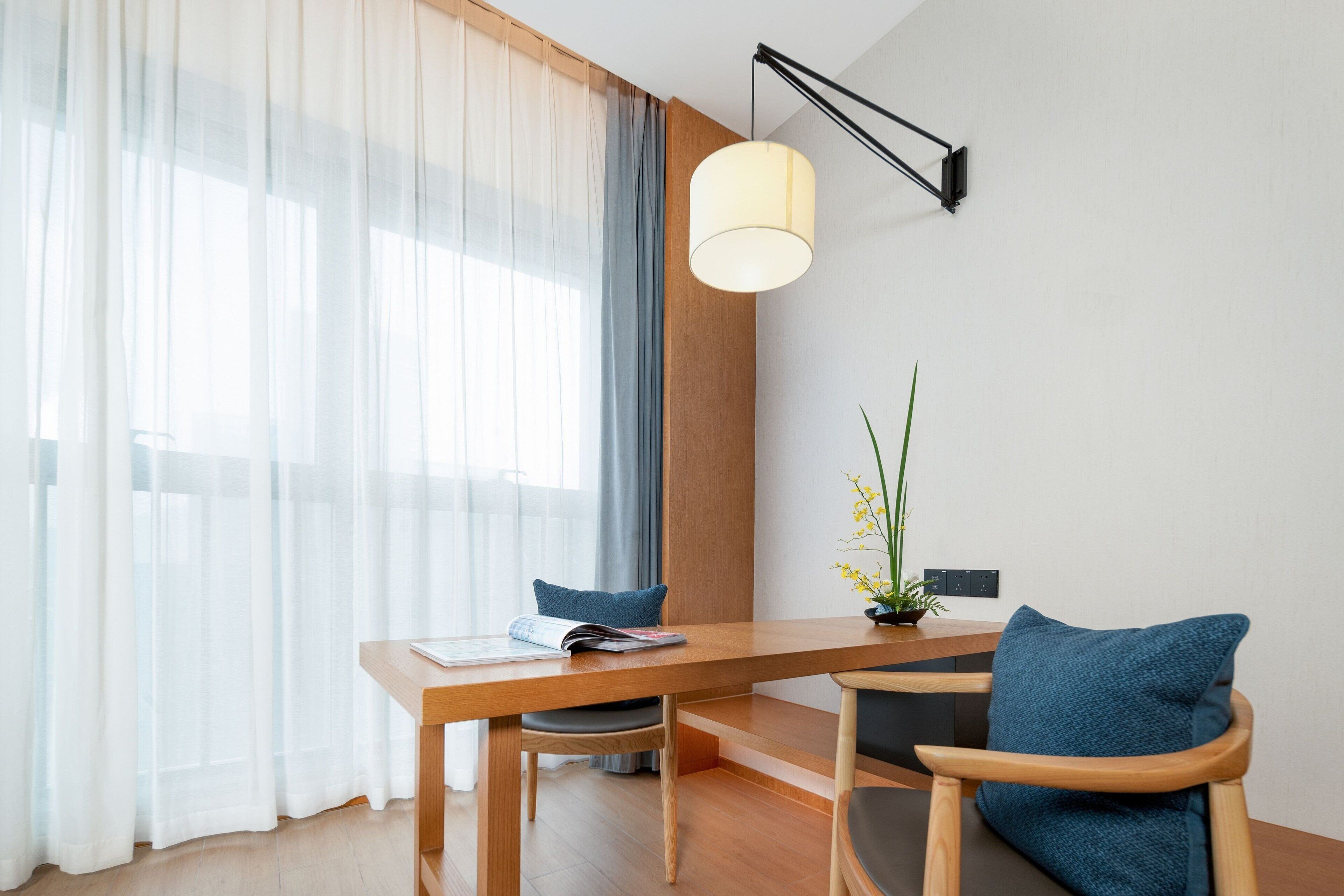 A modern dining area with a wooden table, two chairs, a lamp, and a plant.
