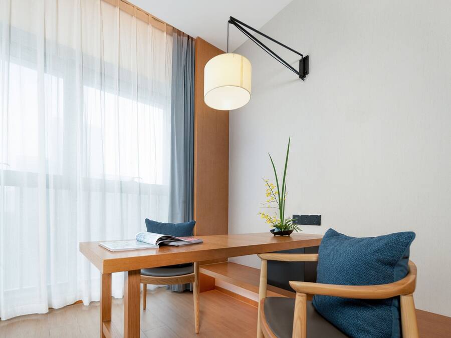 A modern dining area with a wooden table, two chairs, a lamp, and a plant.