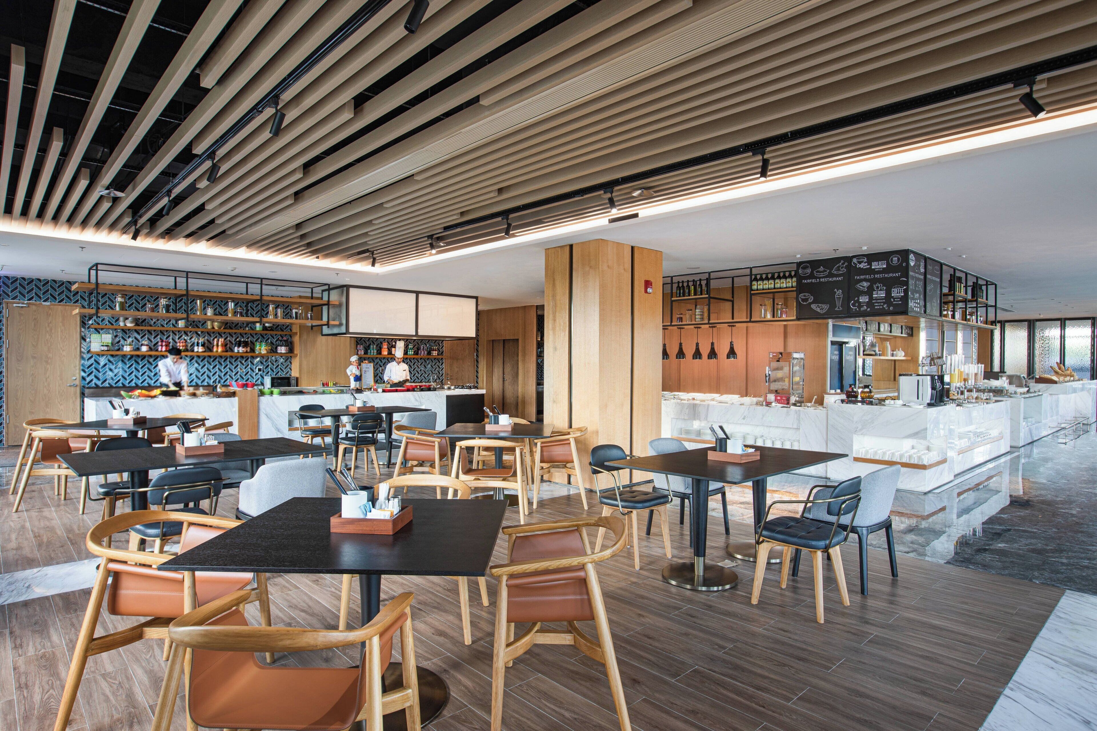 A modern restaurant with wooden furniture, a bar area, and a kitchen visible in the background.