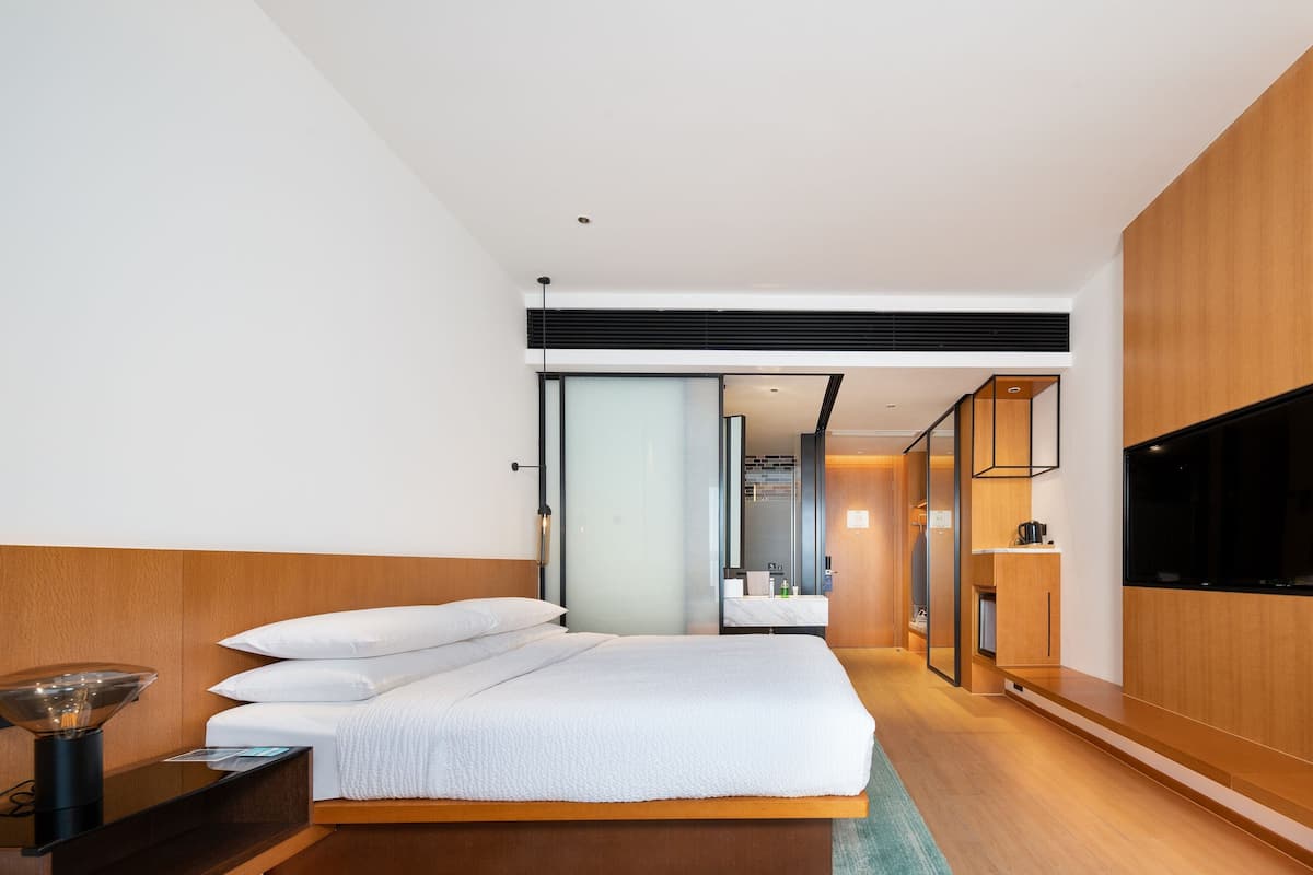A modern hotel room with a large bed, a flat-screen TV, a wooden headboard, and a walk-in closet.