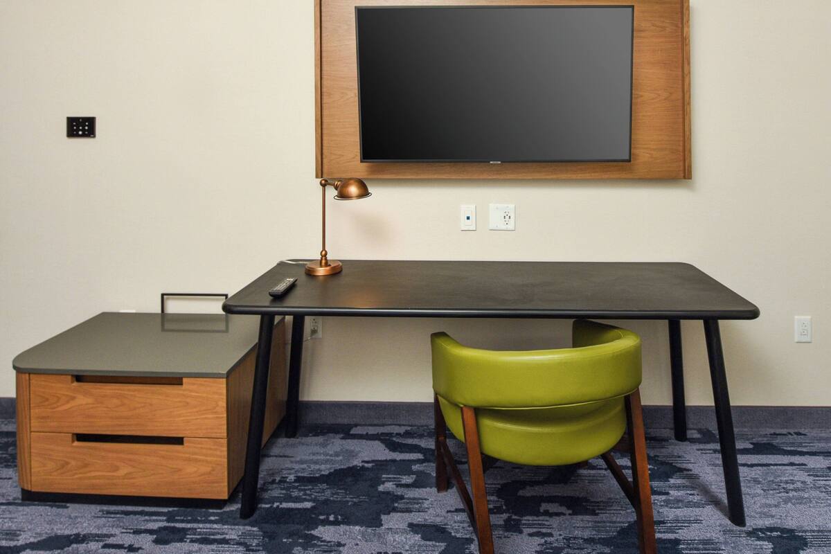 Ein kleiner, ordentlicher Arbeitsplatz mit Schreibtisch, Stuhl, Lampe und einem kleinen Schrank.