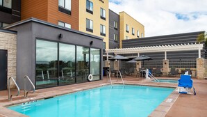 A hotel pool area with clear poolside chairs, a lifeguard stand, and a covered seating area.