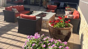 An outdoor patio area with wicker furniture, large planters with flowers, and a glass door leading to a covered seating area.