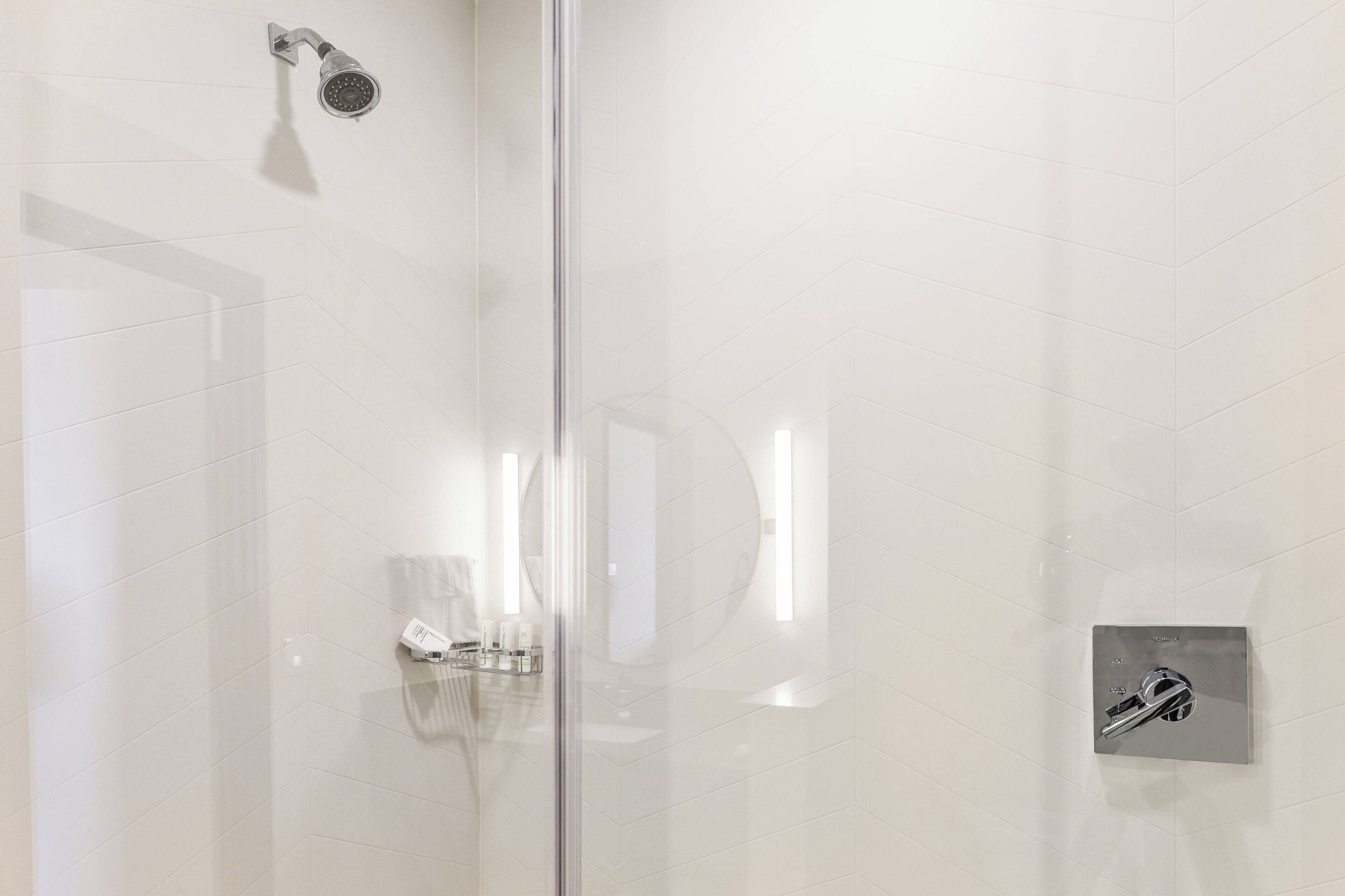 Un baño moderno con cabina de ducha de vidrio, ducha de mano y grifo empotrado.