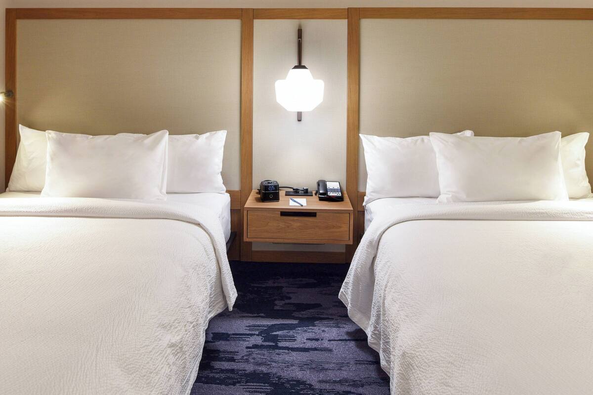 Ein Hotelzimmer mit zwei Betten, einem Nachttisch mit Lampe, einer Uhr und einem Telefon.