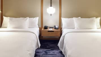 A hotel room with two beds, a nightstand with a lamp, a clock, and a phone.