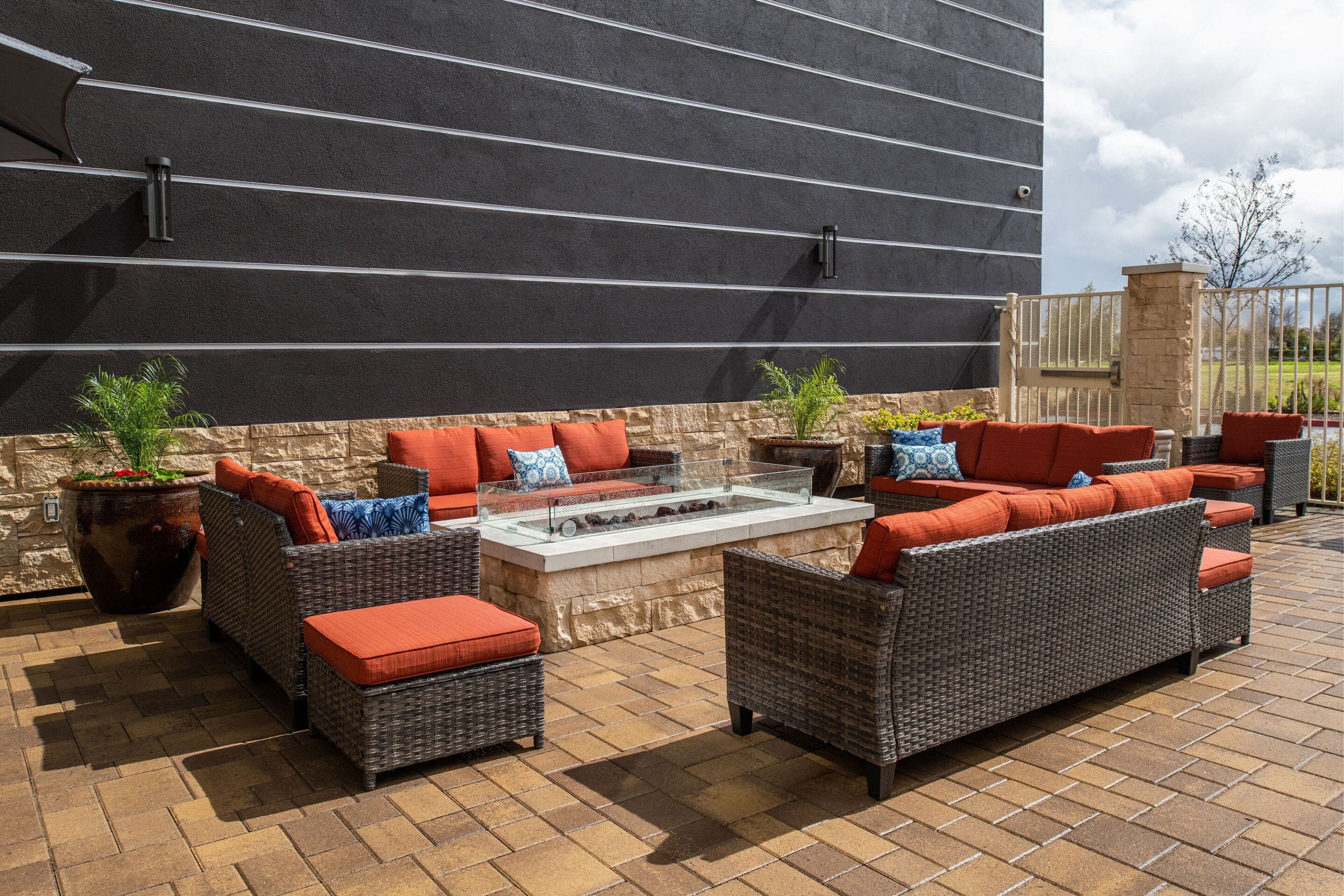 An outdoor patio with wicker furniture, a fire pit, and potted plants.