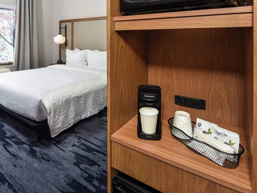 A hotel room with a neatly made bed, a coffee maker, a cup, and a tray with a bag and a box.