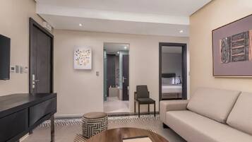 Una habitación de hotel moderna con sofá, televisión, mesa de centro y un cuadro en la pared.