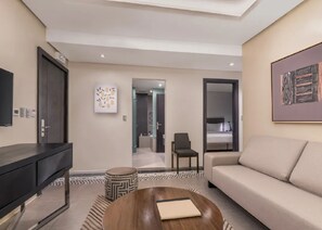 Una habitación de hotel moderna con sofá, televisión, mesa de centro y un cuadro en la pared.