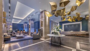 Un moderno vestíbulo de hotel con mostrador de recepción, zona de estar y lámparas geométricas originales.