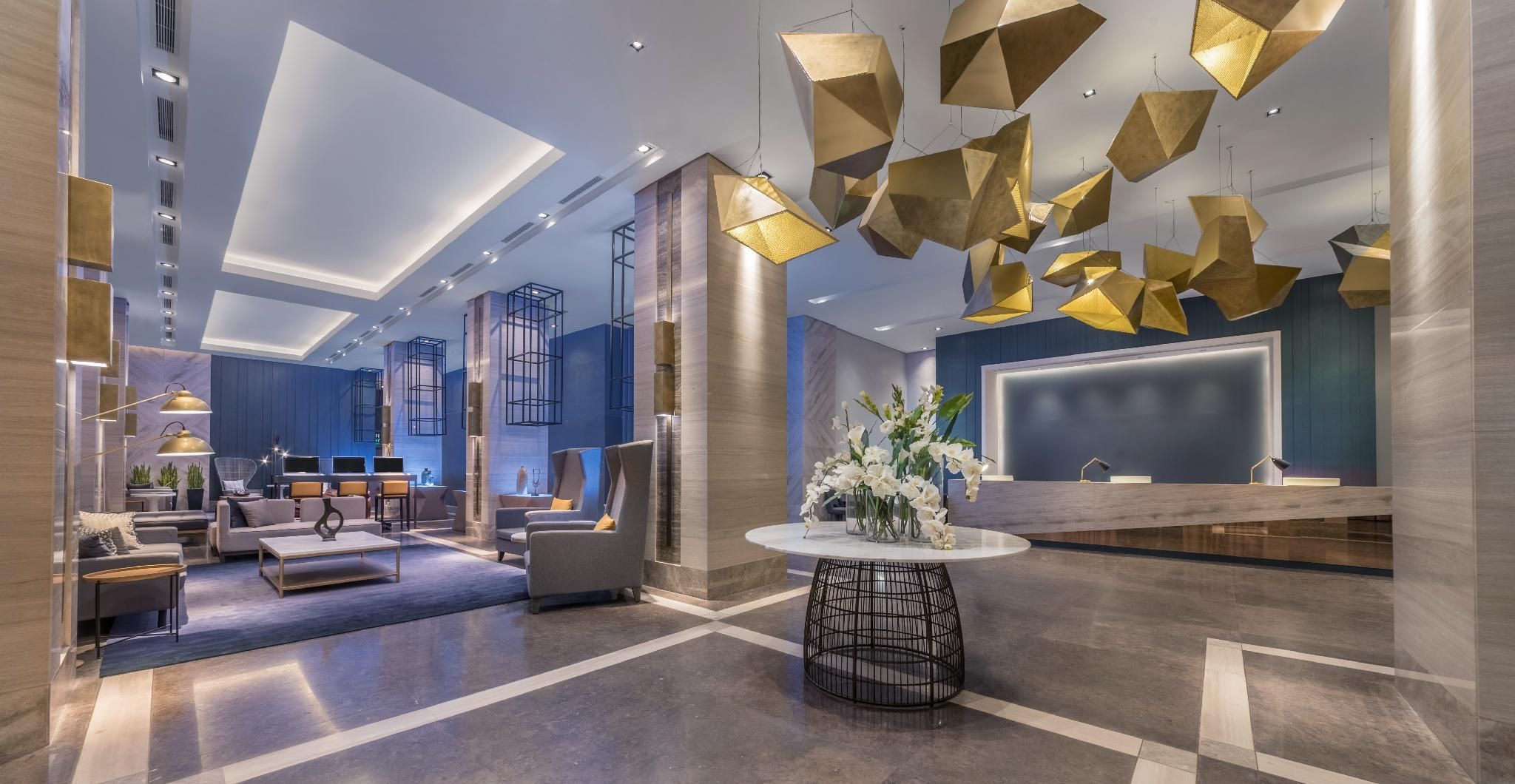 A modern hotel lobby with a reception desk, seating area, and unique geometric light fixtures.