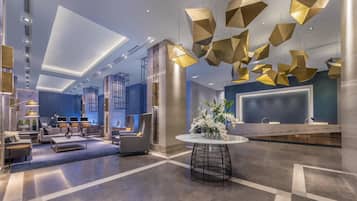 A modern hotel lobby with a reception desk, seating area, and unique geometric light fixtures.