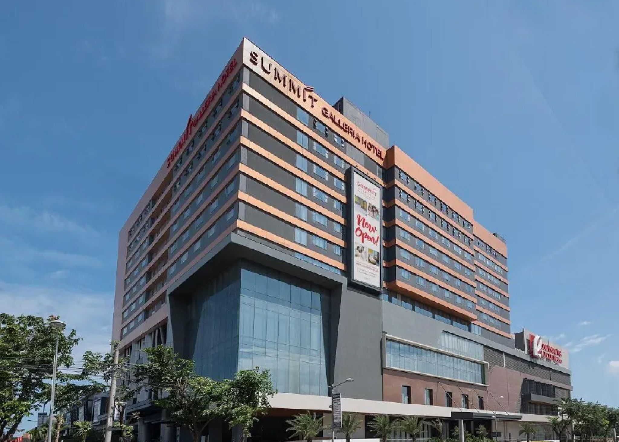 Un hotel de varios pisos con un diseño moderno, que presenta un letrero destacado que dice 'Summit' y un cartel anunciando 'Abierto ya'.