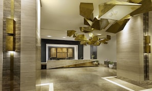 A modern reception area with a geometric light fixture, a reception desk, and a decorative wall panel. - Summit Galleria Cebu (Cebu City)