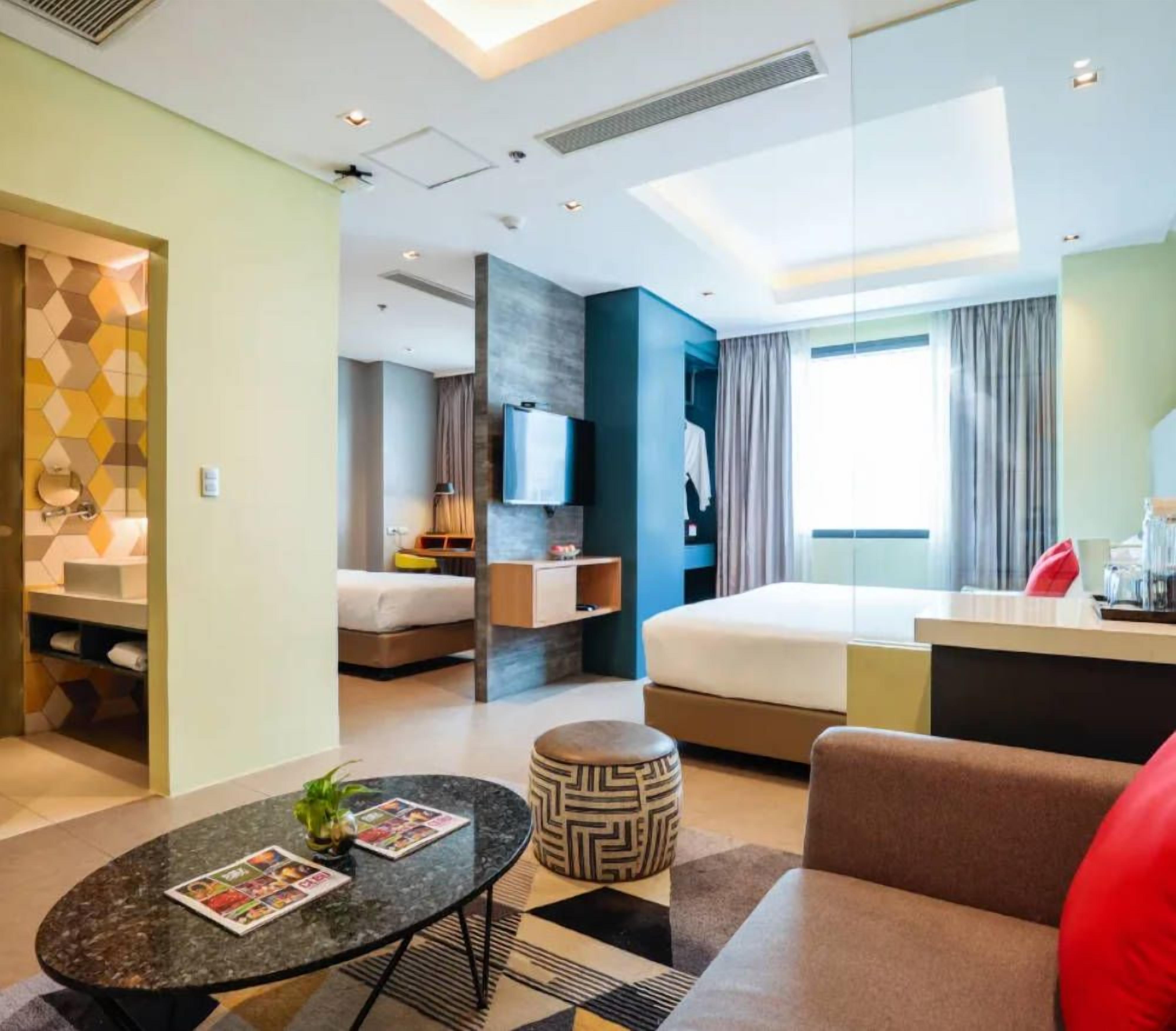 A modern hotel room with a bed, a desk, a TV, and a bathroom visible through an open door.
