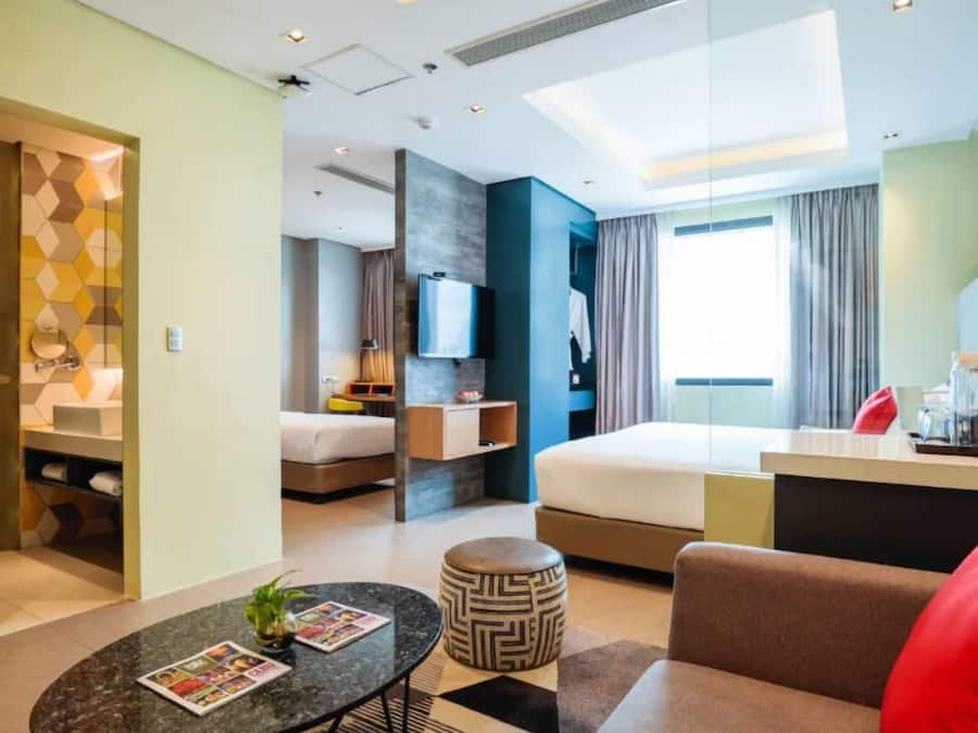 A modern hotel room with a bed, a desk, a TV, and a bathroom visible through an open door.