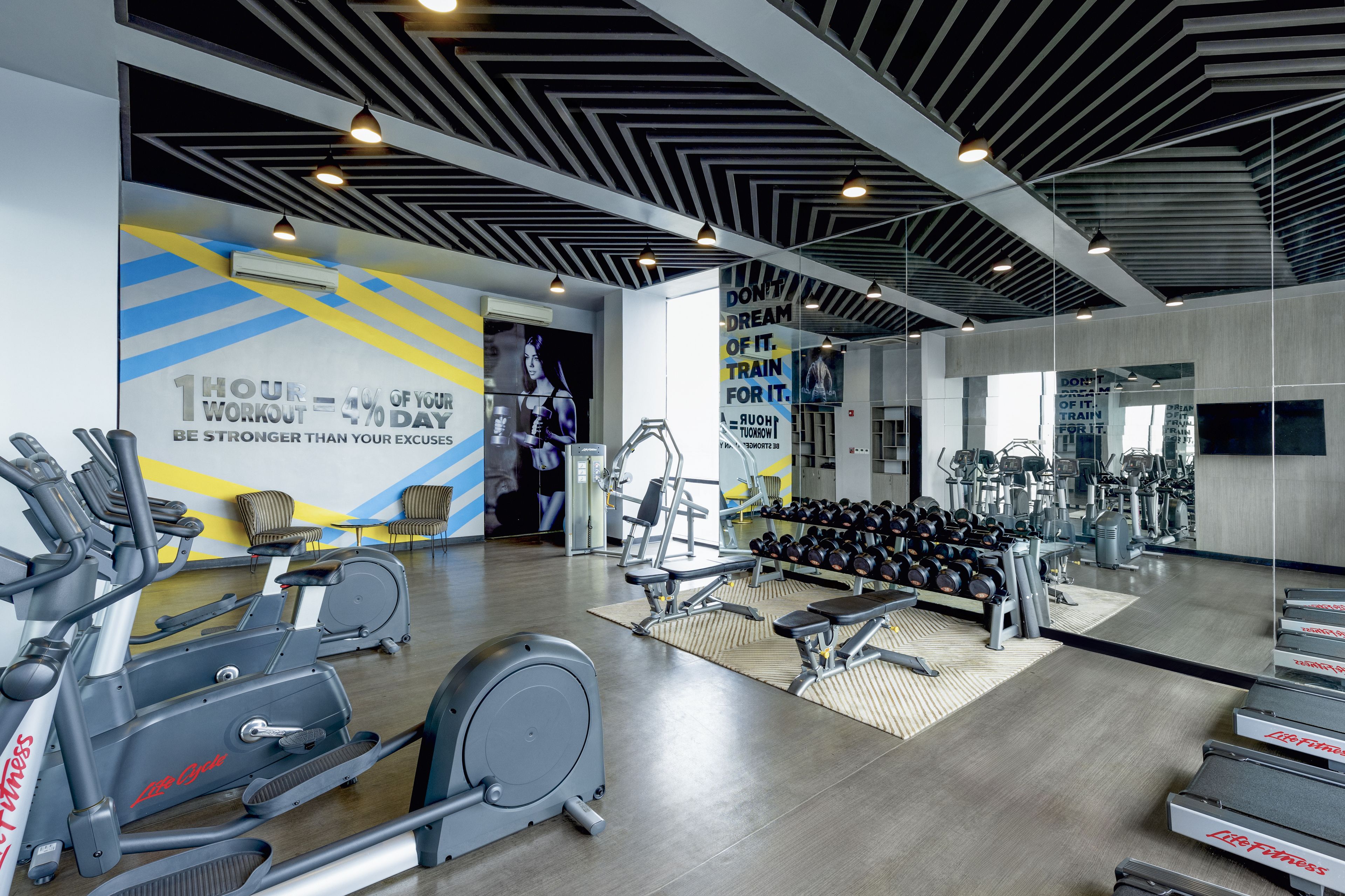 A modern gym with cardio machines, free weights, and motivational posters.