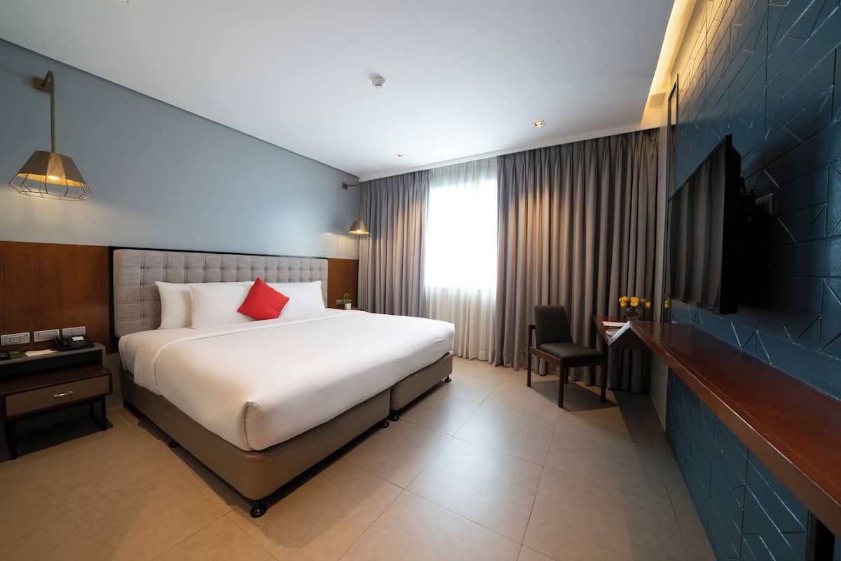 A modern hotel room with a large bed, a desk, and a TV mounted on the wall.